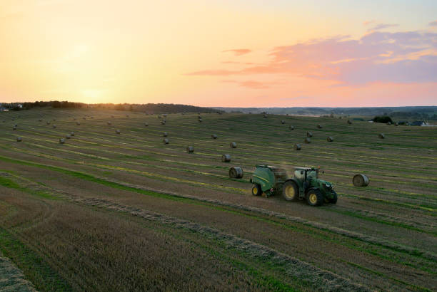 John Deere Tractor 6715R with John Deere V461R round baler making Hay Bales in an agricultural field. stock photo