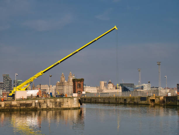A John Sutch mobile crane operating at the Alfred Dock lock gates in Birkenhead, Wirral, UK. The Liverpool waterfront including the Three Graces appears in the background. A John Sutch mobile crane operating at the Alfred Dock lock gates in Birkenhead, Wirral, UK. The Liverpool waterfront including the Three Graces appears in the background. liverpool docks and harbour building stock pictures, royalty-free photos & images