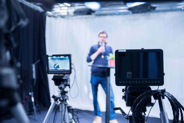 Journalist in a television studio is talking into a microphone, blurry film cameras stock photo