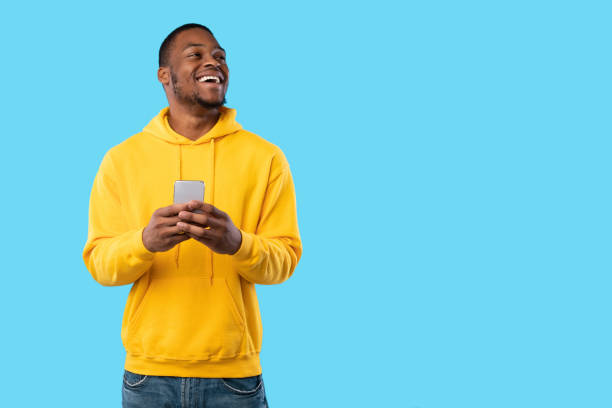 Joyful African Man Using Cellphone Texting Looking Aside, Blue Background stock photo