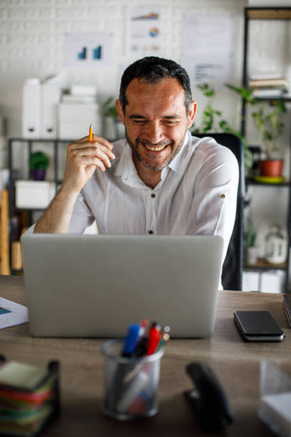 Joyful businessman sitting at his desk, laughing during a video call with a business partner stock photo