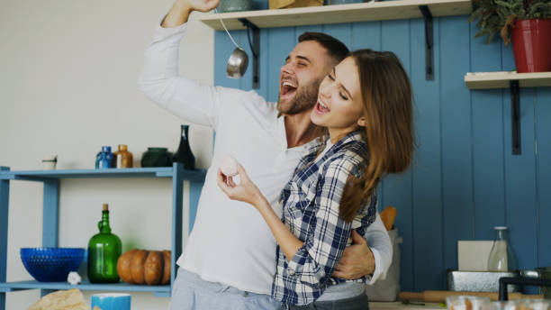 Joyful couple have fun dancing and singing in the kitchen at home in the morning stock photo