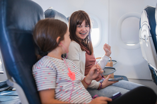 Teenage girls sitting on an airplane and laughing when holding smartphones