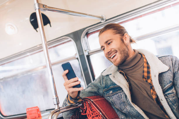 messagerie d'homme de hipster joyeux par le téléphone dans le bus - smartphone car photos et images de collection
