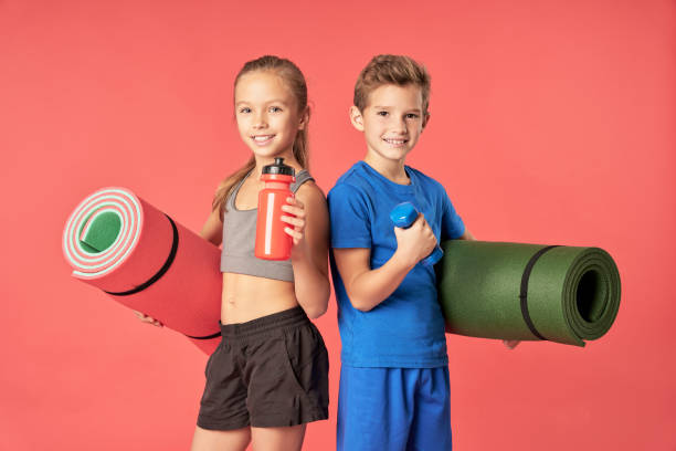 Joyful kids with sports equipment standing against red background stock photo