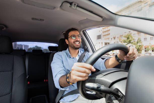 Joyful middle-eastern man driving car, shot from front pannel stock photo