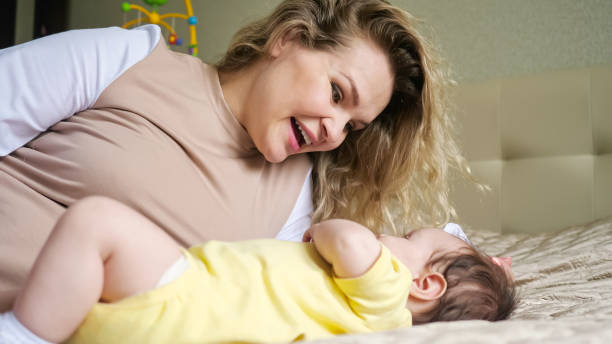 Joyful mother with loose curly hair plays with baby on bed stock photo
