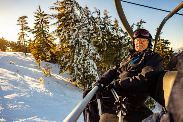 joyful senior caucasian man, enjoy the cable car ride, at the ski resort - posing with ski stockfoto's en -beelden