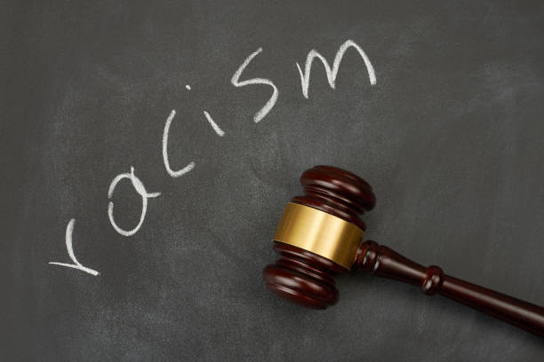 Judge gavel on blackboard background writing the word "racism". stock photo