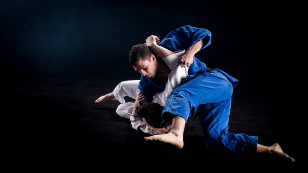 Judokas wrestling on the ground after throw Two judokas in blue and white kimonos wrestling on the ground during a sparring duel. Black background. brazilian culture stock pictures, royalty-free photos & images