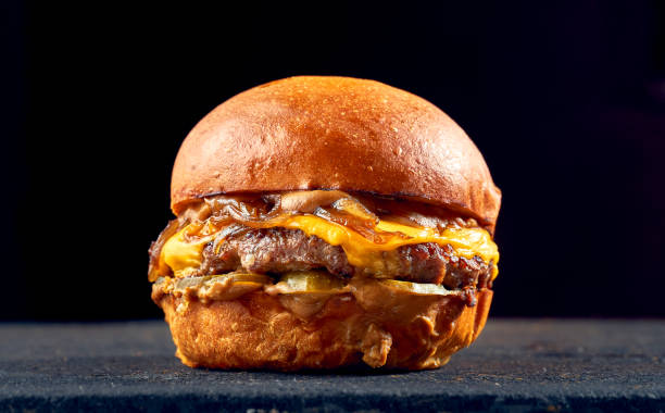 Juicy burger with beef, cheese, caramelized onions and tomato, sauce on a dark background. stock photo