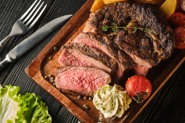 Juicy steak with fragrant butter. Sliced Ribeye Steak with Potatoes, Onions and Baked Cherry Tomatoes stock photo