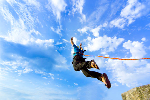 Jump rope from a high rock in the mountains. The first jump off the cliff with a safety rope. cliff jumping stock pictures, royalty-free photos & images