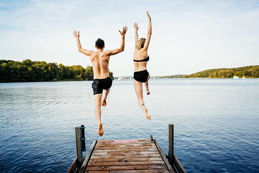 Happy couple jumping into the water from a jetty