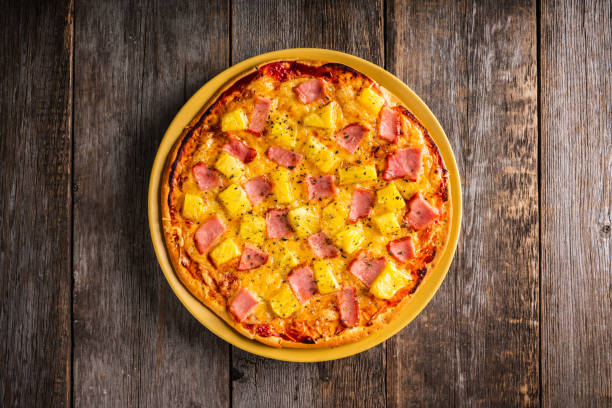Just baked hawaiian pizza with freshly chopped pineapple and ham on the rustic wooden background. Selective focus. stock photo