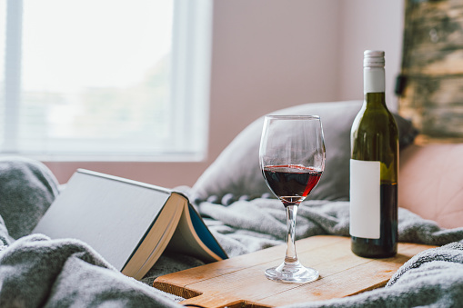 Shot of a glass of red wine and a book on the bed at home