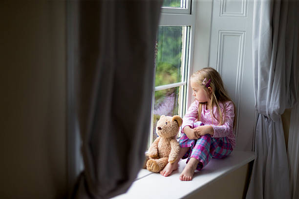Just wanting a friend to play with. Little girl sits on a window sill alone with her teddy. She is looking out of the window. window sill photos stock pictures, royalty-free photos & images