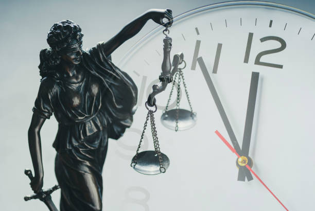 Justice holding the scales of justice and law Silver statuette of Justice holding the scales of justice and law enforcement in front of a clock dial in a close up conceptual composite image deadline stock pictures, royalty-free photos & images