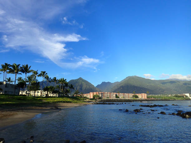 Kahului Bay with Hotel, coconut trees, and Iao Valley and surrounding mountains in the distance on West Maui on a beautiful day. stock photo
