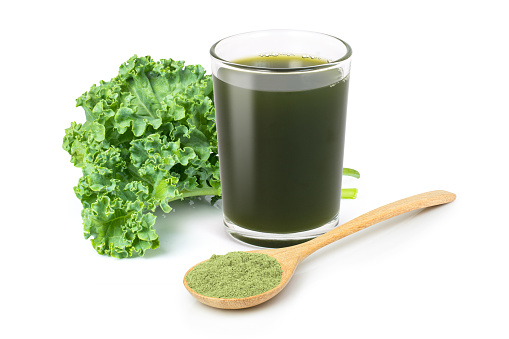 Kale powder in wooden spoon with glass of green smoothie juice and fresh kale vegetable isolated on white background.