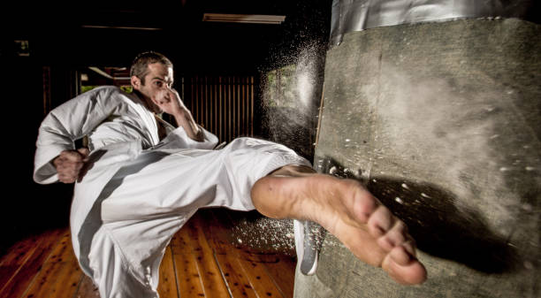 Karate kick into punching bag A powerful side kick into a punching bag in a dojo with the force of the kick shown by dust and powder releasing from the bag around the impact area. "martial arts" stock pictures, royalty-free photos & images