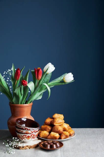 Kazakh national bowls kese, fried bread baursaks and tulips during Nauryz festival on blue background stock photo