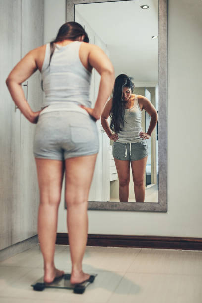 Keeping a close eye on her weight Shot of a young woman weighing herself on a scale at home body conscious stock pictures, royalty-free photos & images