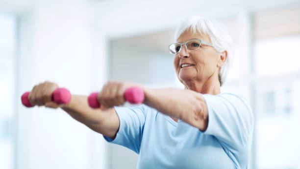 Keeping herself fit and healthy in her latter years Shot of cheerful senior woman working out using dumbbells at home picking up photos stock pictures, royalty-free photos & images
