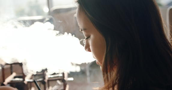Shot of a young woman vaping at home