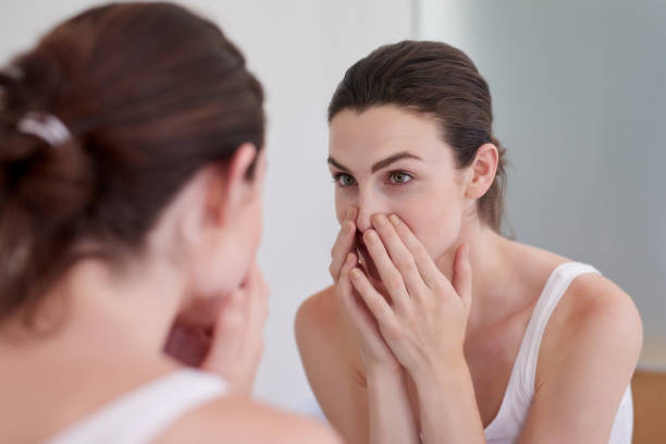 Keeping the health of her skin in check Shot of an attractive young woman inspecting her face in the bathroom mirror imperfection stock pictures, royalty-free photos & images
