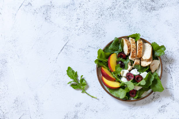Keto diet lunch. Healthy diet salad with arugula, grilled turkey, peach, cherry, feta and vinaigrette dressing on a stone tabletop. Top view flat lay background. Copy space. stock photo