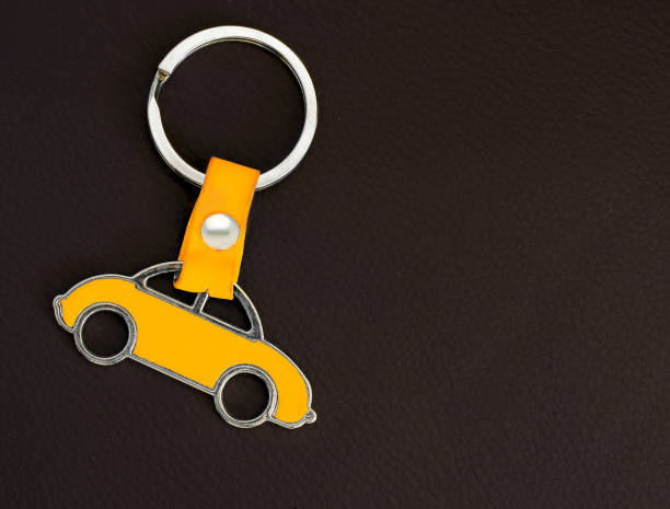 Key chain with yellow car on dark leather pad as background stock photo