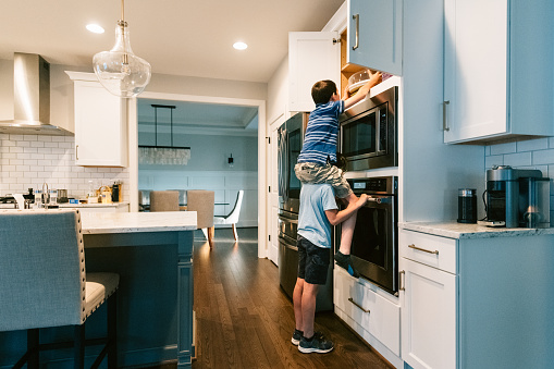 Kid carrying friend of shoulders to help him reach a high cupboard in the kitchen