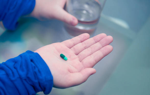 kid hand hold pill supplement antioxidant vitamin mineral capsule with water glass before take medicine capsule for health care stock photo