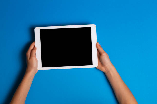 mains d'enfant retenant l'ordinateur blanc de tablette sur le fond bleu clair - fond bleu marine photos et images de collection