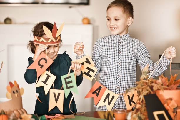 Kid holding paper garland with text Give thanks. Children decorating living room for celebrating Thanksgiving day. stock photo
