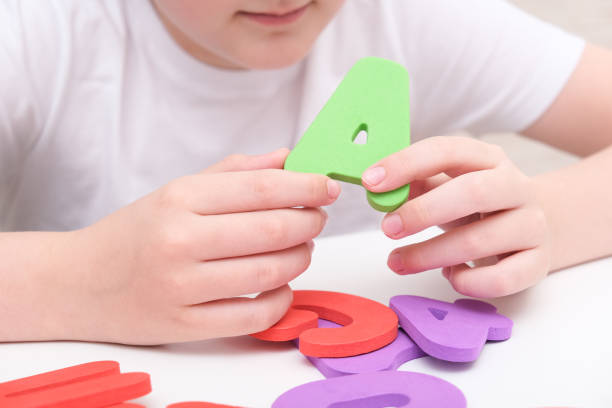 A kid learning letters and alphabet, he is sitting at a table and holding colorful foam letters in hands stock photo