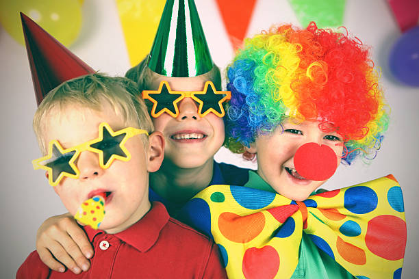 Kids Birthday Party Three boys dressed up in colorful party clothing are celebrating a birthday. One child is wearing a colorful clown wig, a red nose, and a giant bow tie, the other two boys have party hats and funny sunglasses on, one of them is blowing a party blower. This is a tinted, retro style image of the childrens party. clown stock pictures, royalty-free photos & images