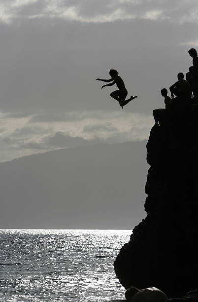 Kids Cliff Jumping and Diving in Hawaii Teenagers leaping off Black Rock in Kaanapali, Maui. One boy is midair, his limbs and wild hair silhouetted 25 feet above the ocean. cliff jumping stock pictures, royalty-free photos & images