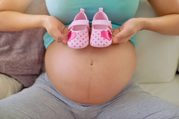 Closeup shot of a pregnant woman holding a pair of pink baby shoes...