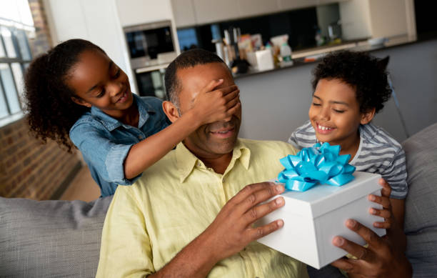 Kids surprising their father with a gift for Father's Day Happy African American kids surprising their father with a gift at home and covering his eyes - Father's Day concepts fathers day stock pictures, royalty-free photos & images