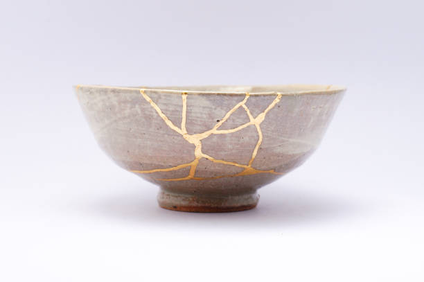 Kintsugi Antique broken Japanese bowl repaired with gold. Kintsugi beige bowl. Gold cracks restoration on old Japanese pottery restored with the antique Kintsugi restoration technique. The beauty of imperfections. japanese pottery repair gold. japanese art of repairing cracks with gold. japanese art of fixing broken pottery imperfection photos stock pictures, royalty-free photos & images