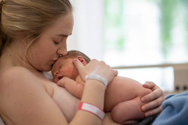 Kissing a newborn A mother is smiling while kissing her beautiful newborn daughter. They are in a hospital bed. childbirth stock pictures, royalty-free photos & images