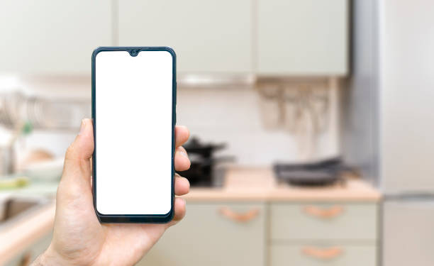 Kitchen background with hand with phone. Blurred home kitchen with blank smartphone screen. Online grocery ordering concept, online food shopping. stock photo