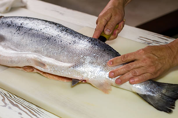Kitchen knife cuts raw fish. Man's hand on raw fish. Kitchen table in...