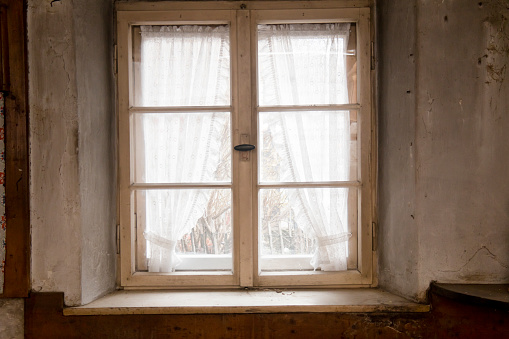 Kitchen window of a 300 years old farmhouse. Window with curtains and view in the garden.