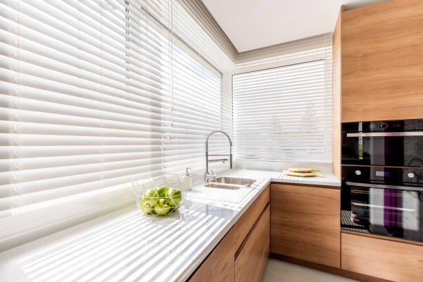 Kitchen with white window blinds Modern bright kitchen interior with white horizontal window blinds, wooden cabinets with white countertop and household appliances roller blinds stock pictures, royalty-free photos & images