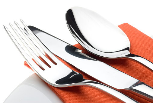 A close up studio shot of a cutlery set on an Orange napkin and china plate with a white background.