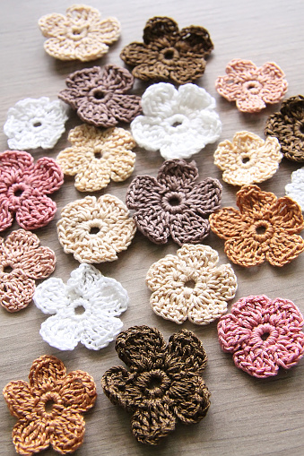 knitted flowers of different sizes and colors on a wooden table. Handmade work.