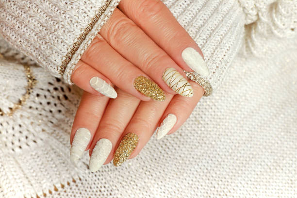 Knitted sand manicure on long oval nails with golden sequins and threads Knitted sand manicure on long oval nails with golden sequins and threads on a woman's hand in a jacket. Winter trend in nail design. artificial nail stock pictures, royalty-free photos & images